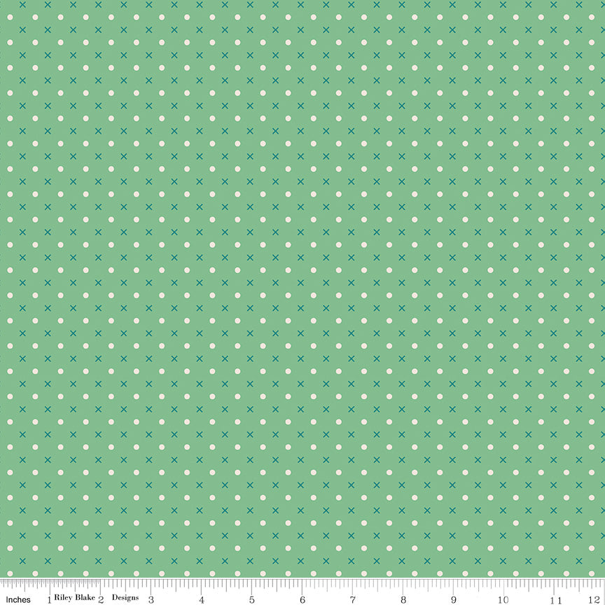 A fabric pattern swatch featuring a sage green background with a repeating motif of small white dots and blue x's, with a ruler at the bottom indicating scale.