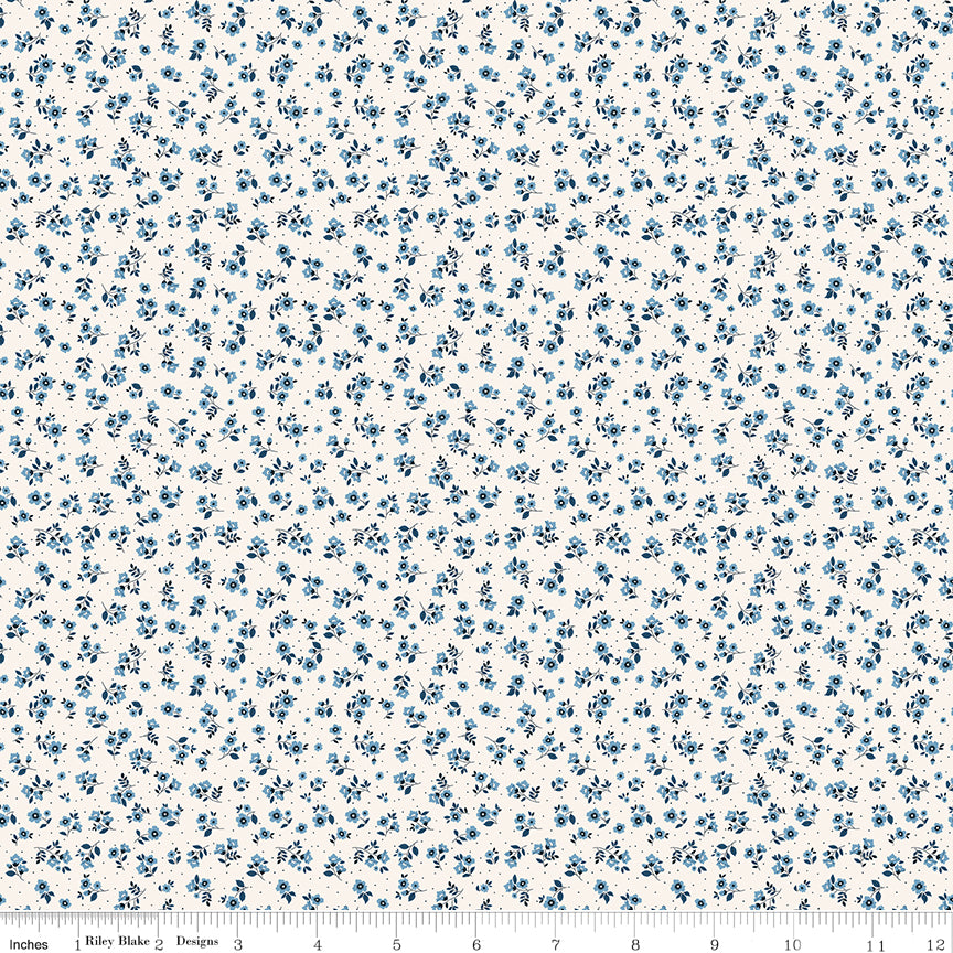 A close-up of a fabric pattern featuring small blue floral motifs scattered across a white background, with a ruler at the bottom edge showing scale.