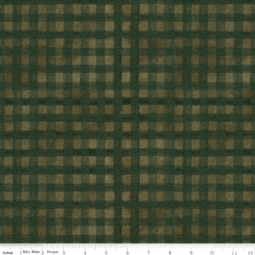 A close-up of a dark green and brown gingham plaid fabric pattern with a white ruler along the bottom edge showing scale.