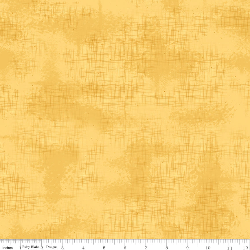 Yellow fabric with thin crosshatched lines and scattered specks, with a ruler along the bottom edge.
