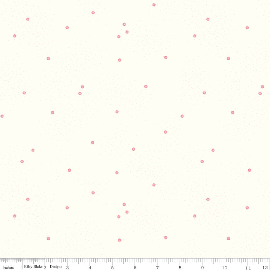 A close-up of a fabric pattern featuring small, scattered dusty pink daisies and dots on a warm off-white background, with a ruler visible along the bottom edge for scale.