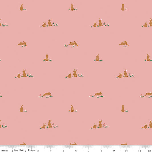 Fabric with a pattern of small bunny illustrations on a pink background with a ruler at the bottom for scale.