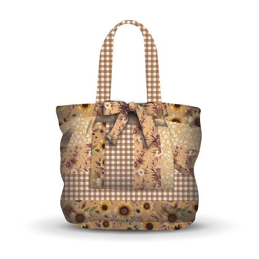 A tote bag featuring a patchwork design of brown and beige gingham, floral prints, and sunflower motifs, with matching gingham handles, shown on a white background.