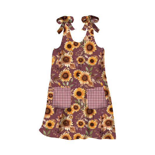 A sleeveless dress-style apron with a brown and yellow sunflower print, featuring two wine-and-white gingham pockets and matching ribbon neck ties, shown on a plain white background.