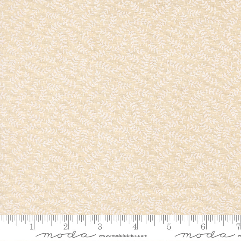 A close-up of a fabric pattern showing a repeating white leafy vine motif on a warm cream-beige background, with a measuring ruler along the bottom edge for scale. The brand name 'Moda' is visible on the ruler watermark.