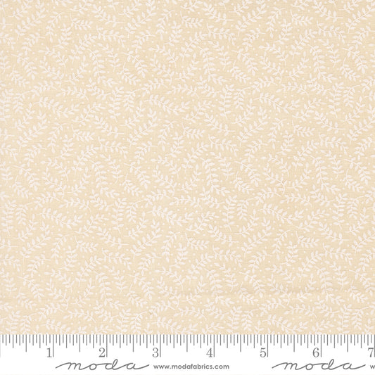 A close-up of a fabric pattern showing a repeating white leafy vine motif on a warm cream-beige background, with a measuring ruler along the bottom edge for scale. The brand name 'Moda' is visible on the ruler watermark.